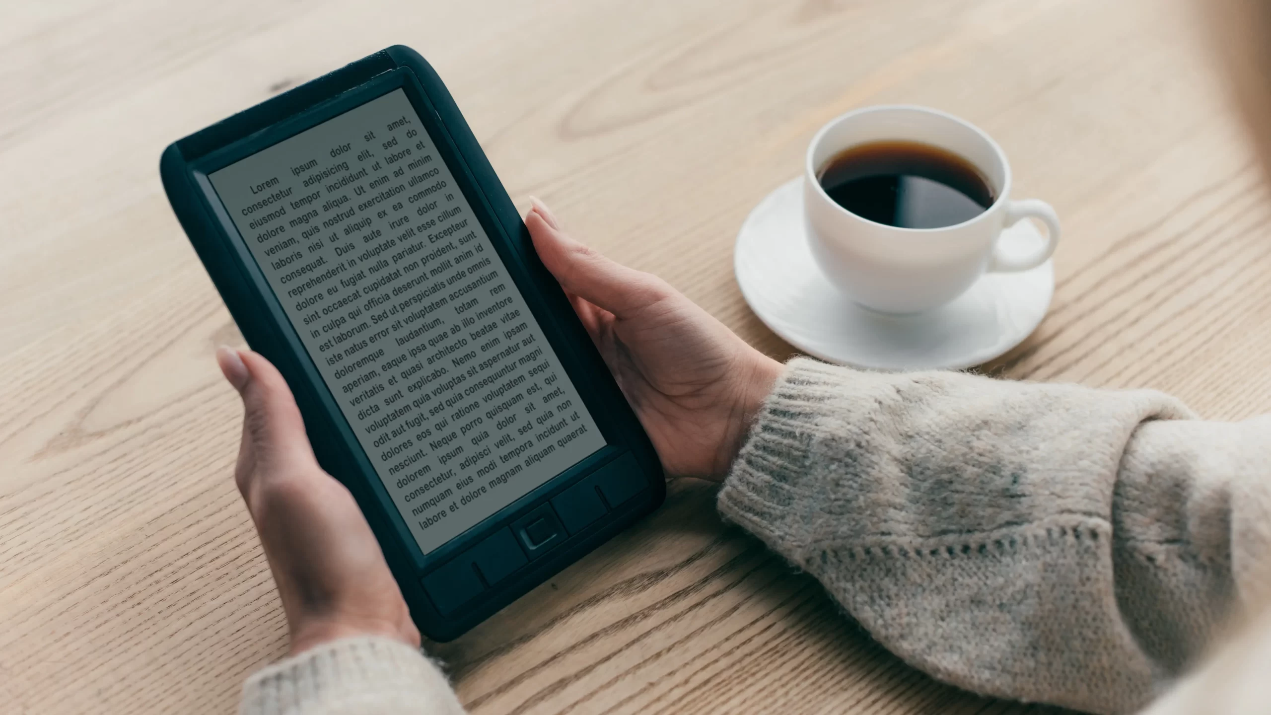 A person holding an ebook and a cup of coffee